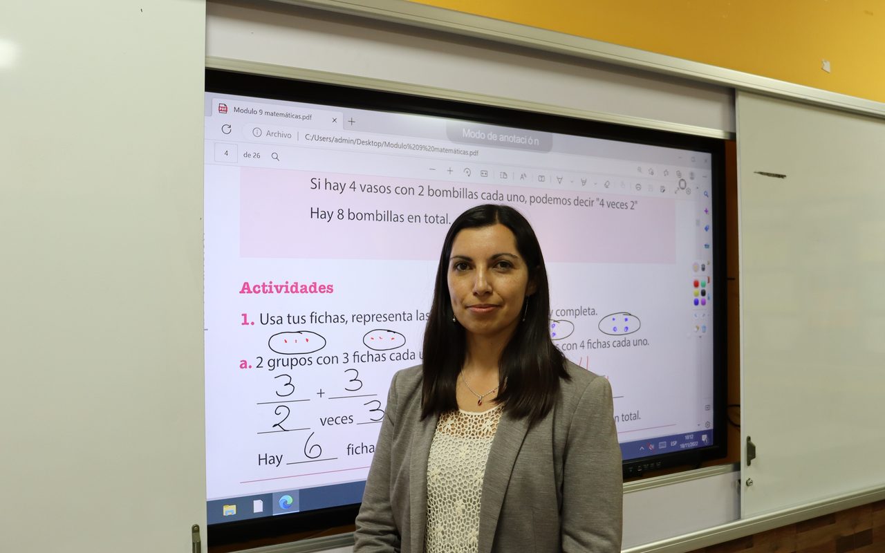 Profesora frente a pantalla Edutouch con guía de matemáticas anotada